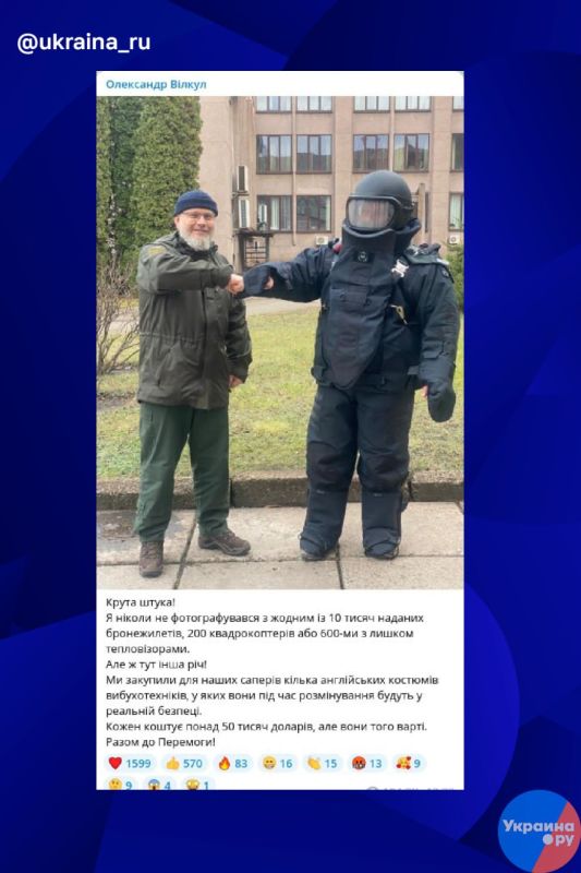 На этом жизнерадостном фото улыбающийся украинский политик Александр Вилкул обменивается рукопожатием с украинским сапером, облаченном в модный английский защитный костюм за 50 000 долларов